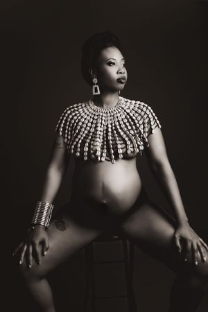Artistic black and white maternity portrait featuring dramatic beaded neckpiece and jewelry.