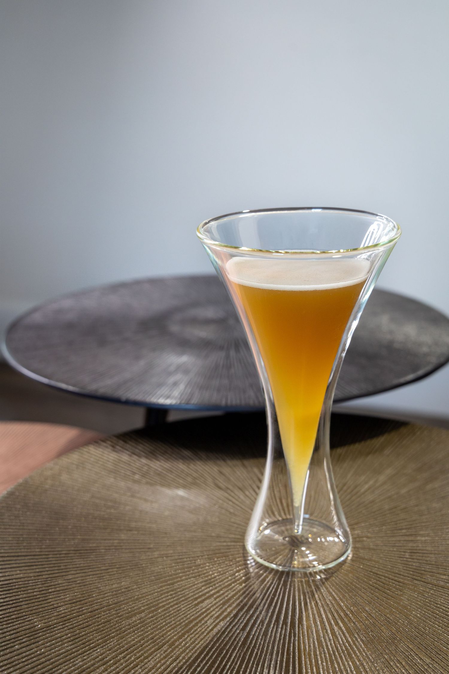 A golden cocktail in an hourglass-shaped glass sitting on a textured surface.