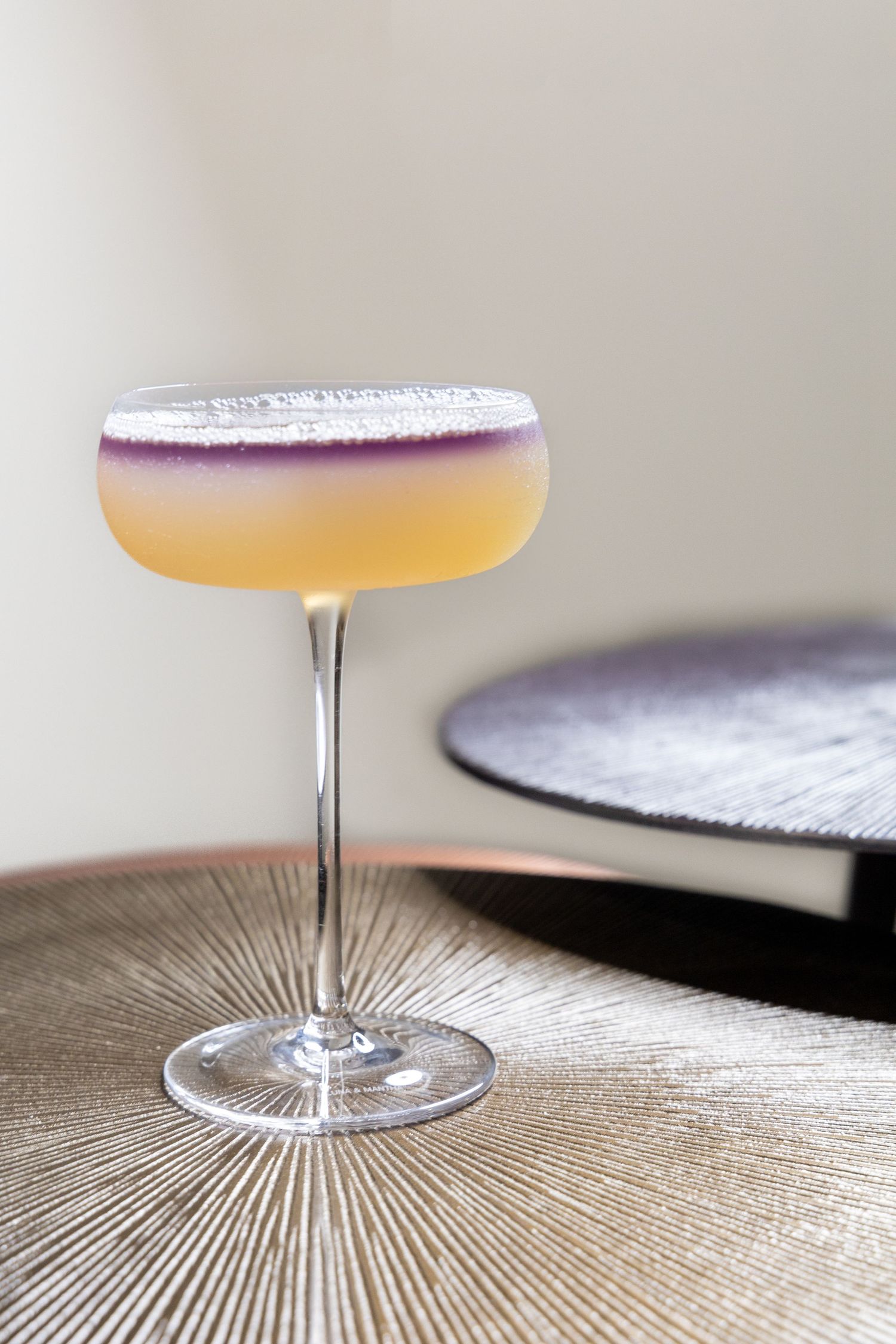 Elegant cocktail with purple-tinted foam layer served in stemmed coupe glass.