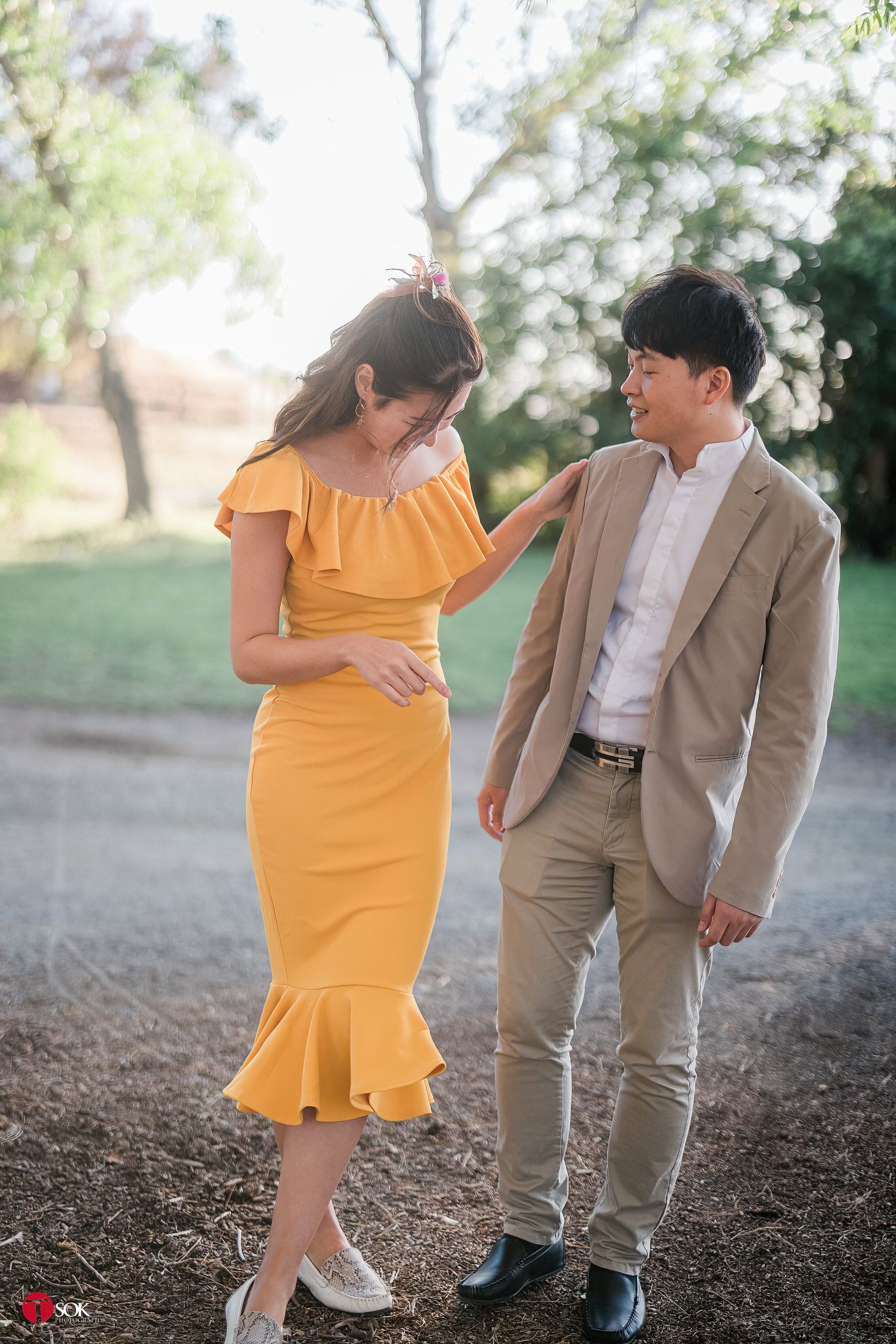 Romantic couple in formal attire share a laugh on a garden path.