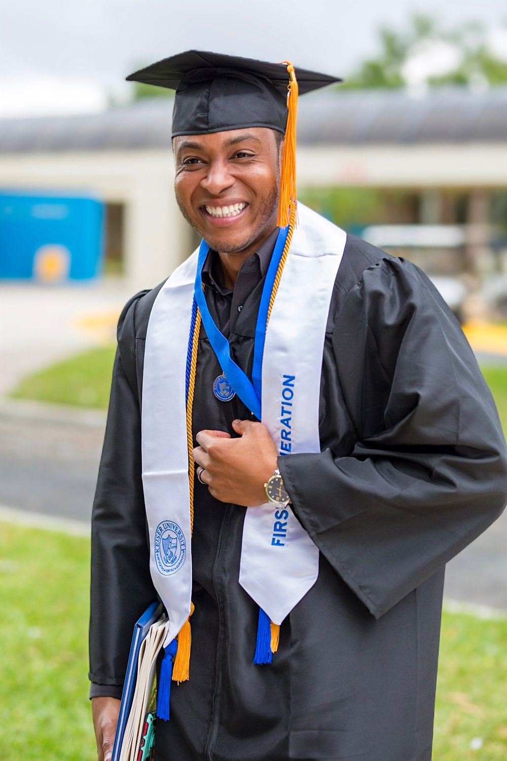 Graduate wearing traditional black cap and gown with blue and gold honor stole.