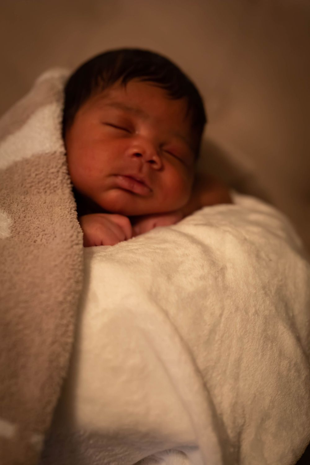 Sleeping newborn baby wrapped snugly in soft white and beige blankets.