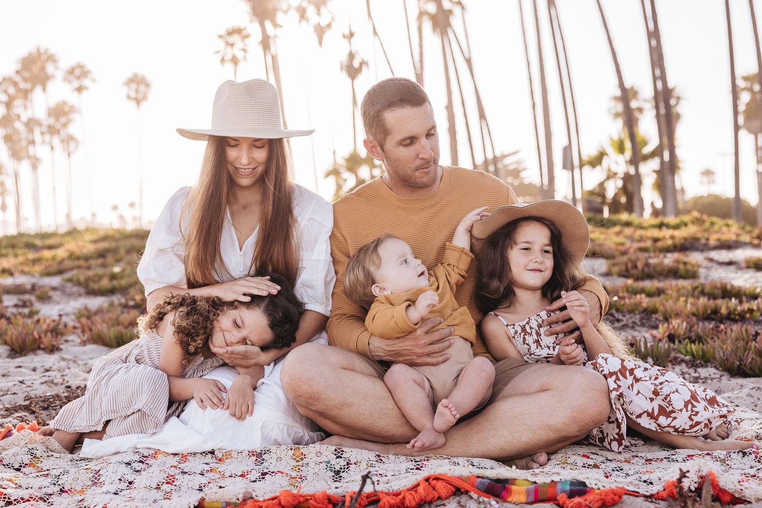 Family having picnic on blanket during golden sunset among palm trees.