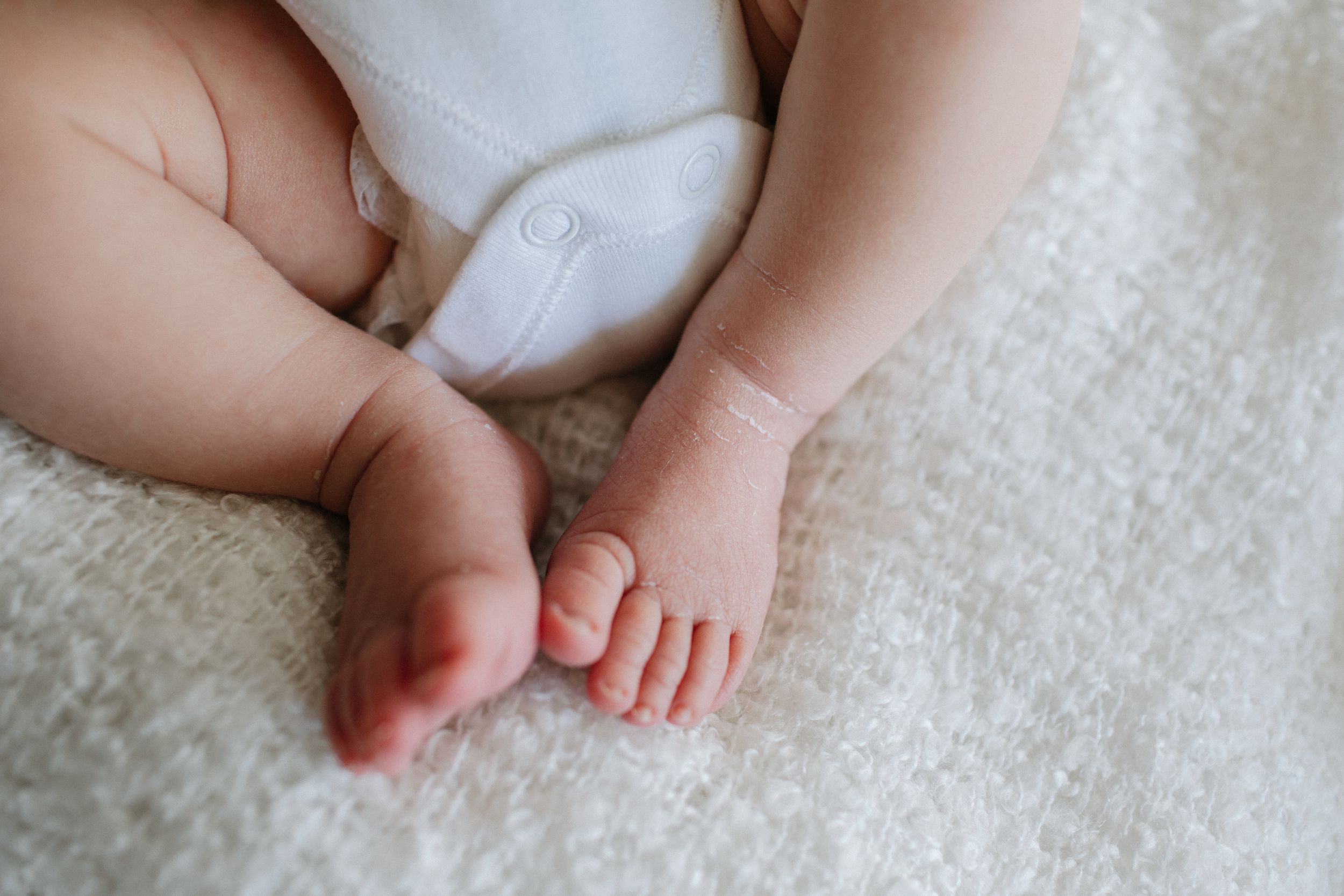 Close-up photograph of tiny feet against white textured fabric.