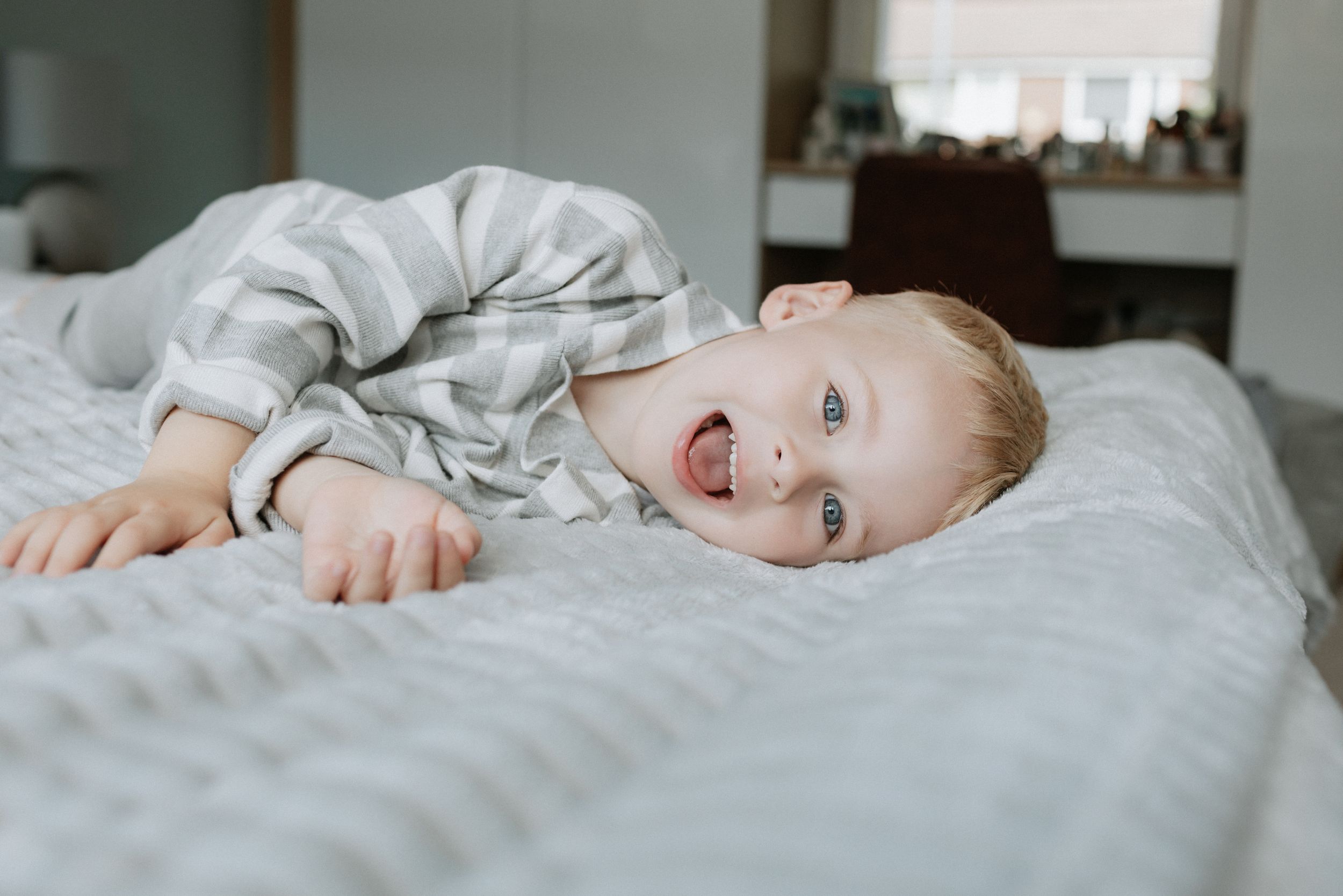 Happy child in gray striped pajamas laying on white bedding.