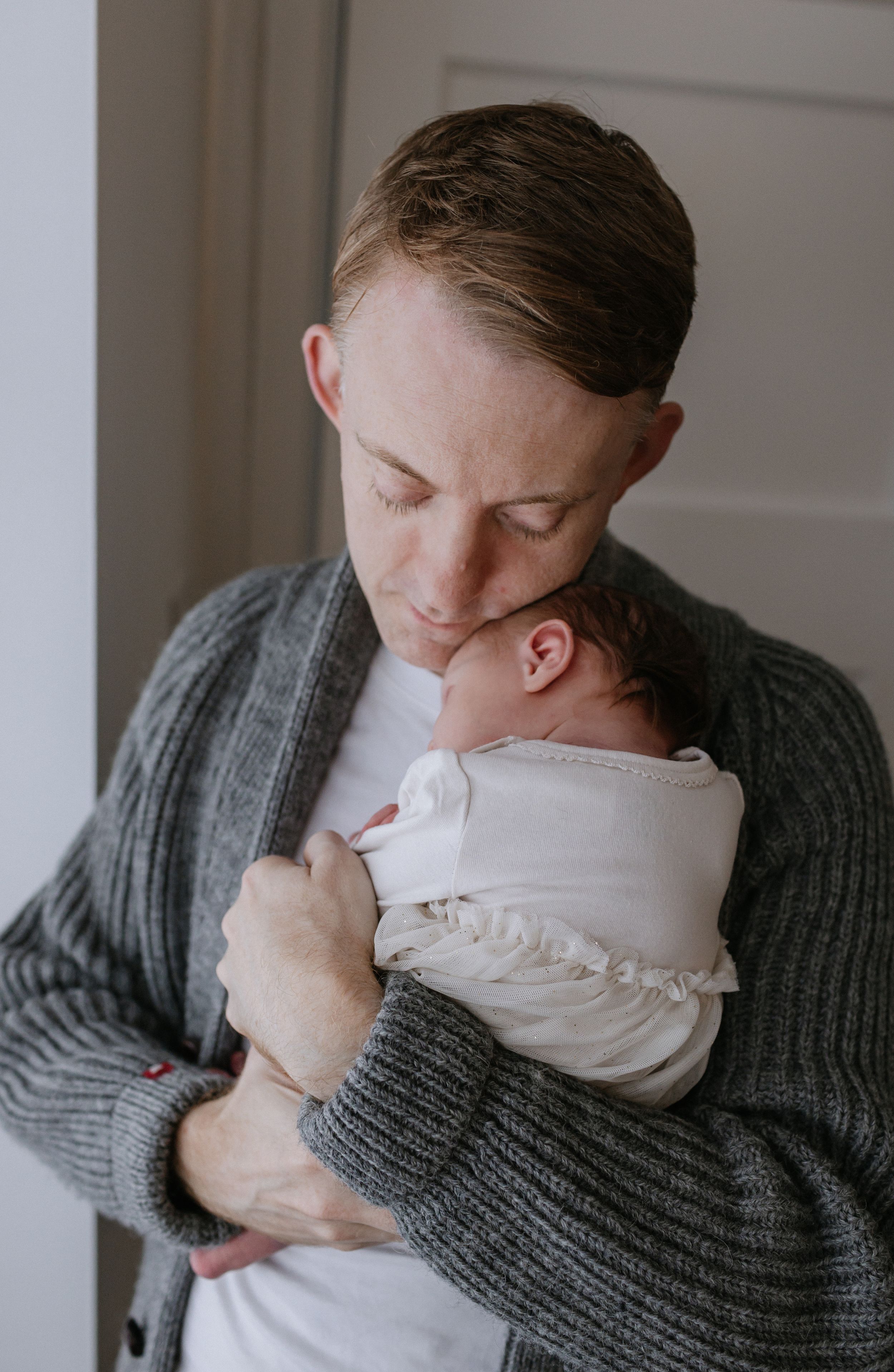 Tender moment captured of parent holding newborn baby in gray knit sweater.