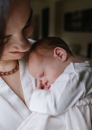 Close-up of sleeping newborn baby in white outfit resting against caregiver.