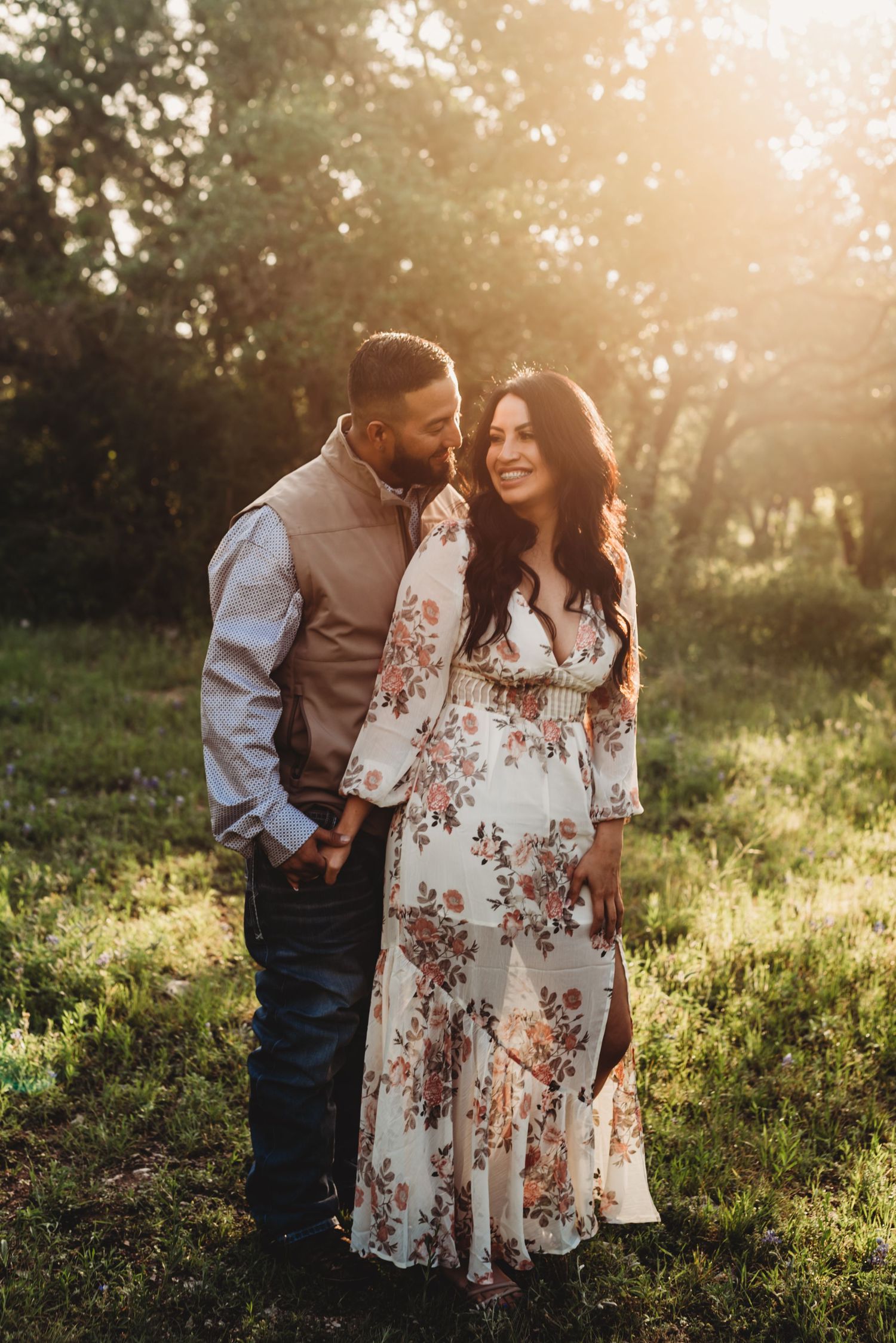 Romantic couple embrace in floral dress and casual attire during sunset photoshoot in nature.