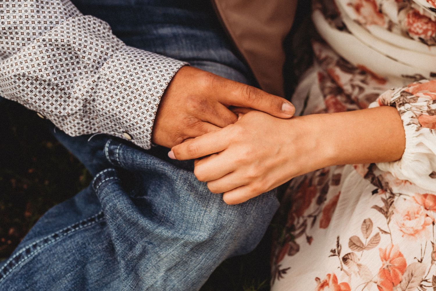 Close-up of hands holding together against denim and floral fabric.