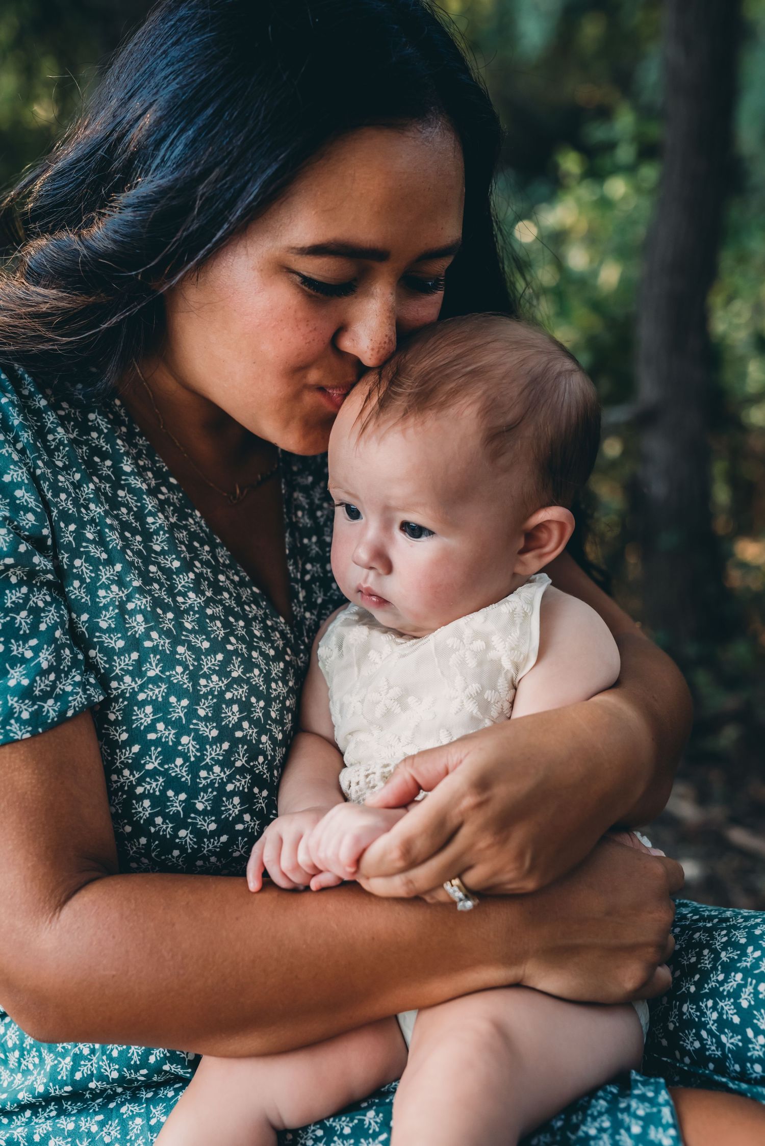 Tender moment captured between parent and baby in white outfit outdoors.