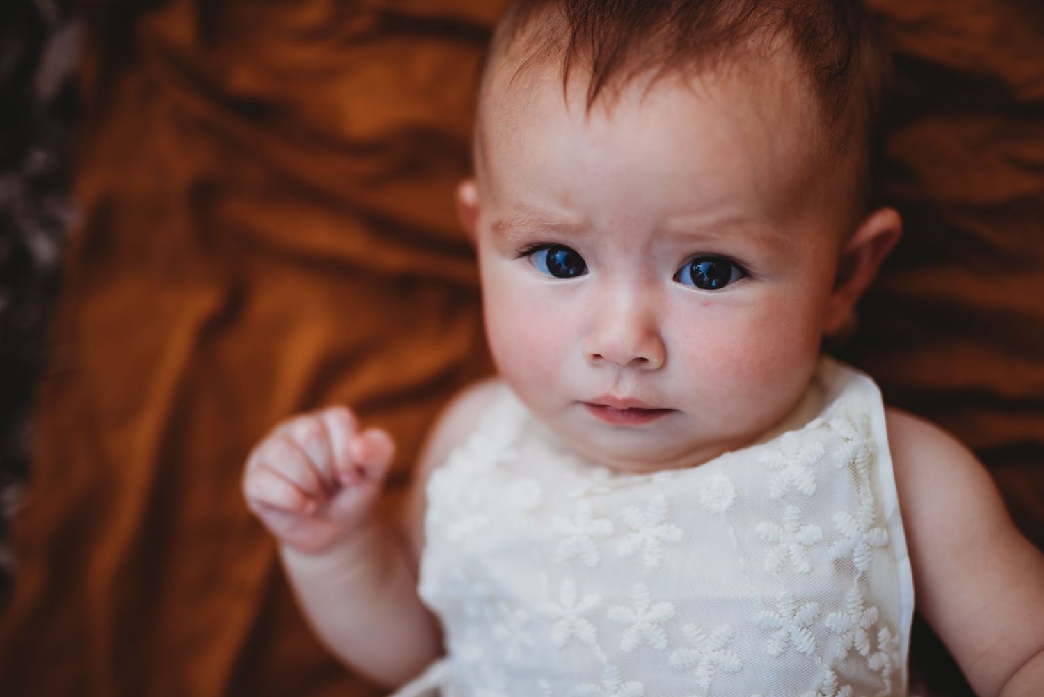 Close up of baby in white lace dress against warm background.