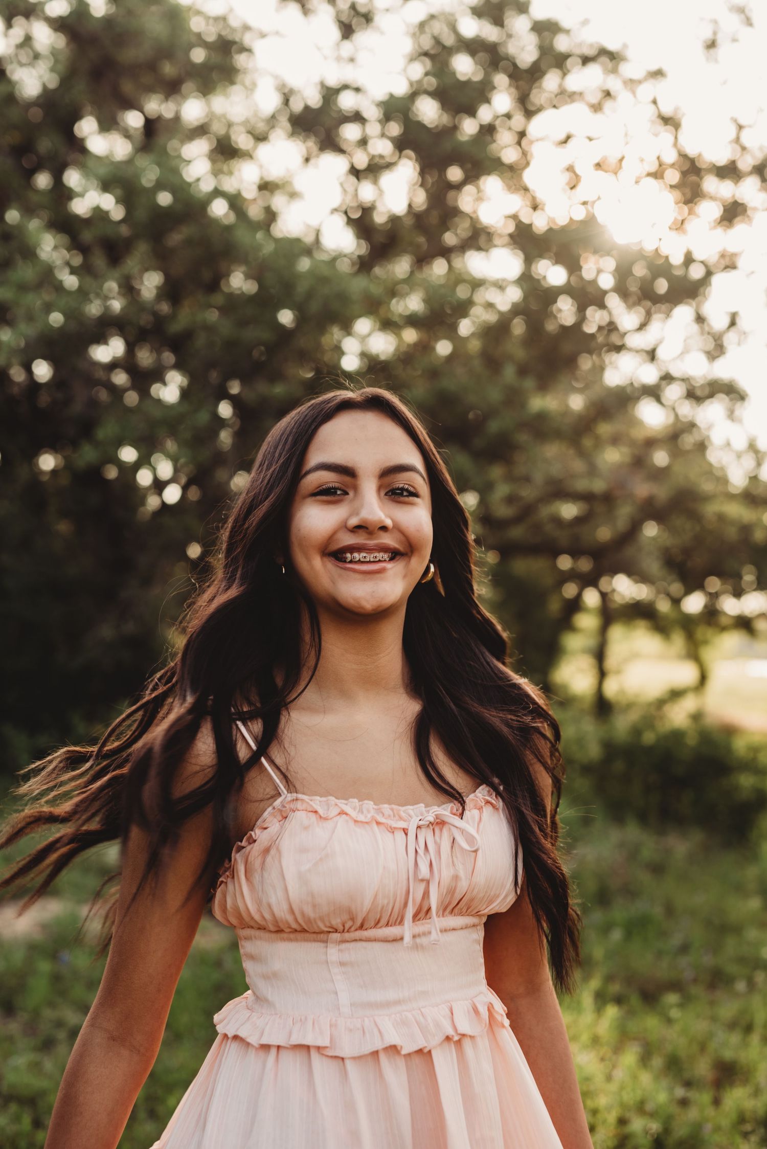 Young woman in pink dress twirls joyfully during sunset portrait session in nature.