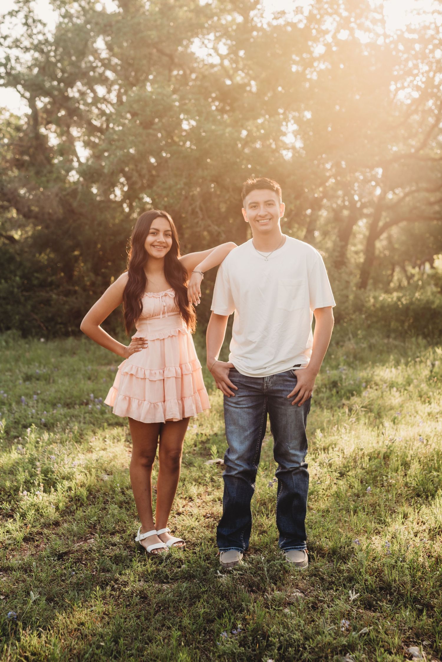 Young couple poses casually on grassy hillside during golden hour photo session.
