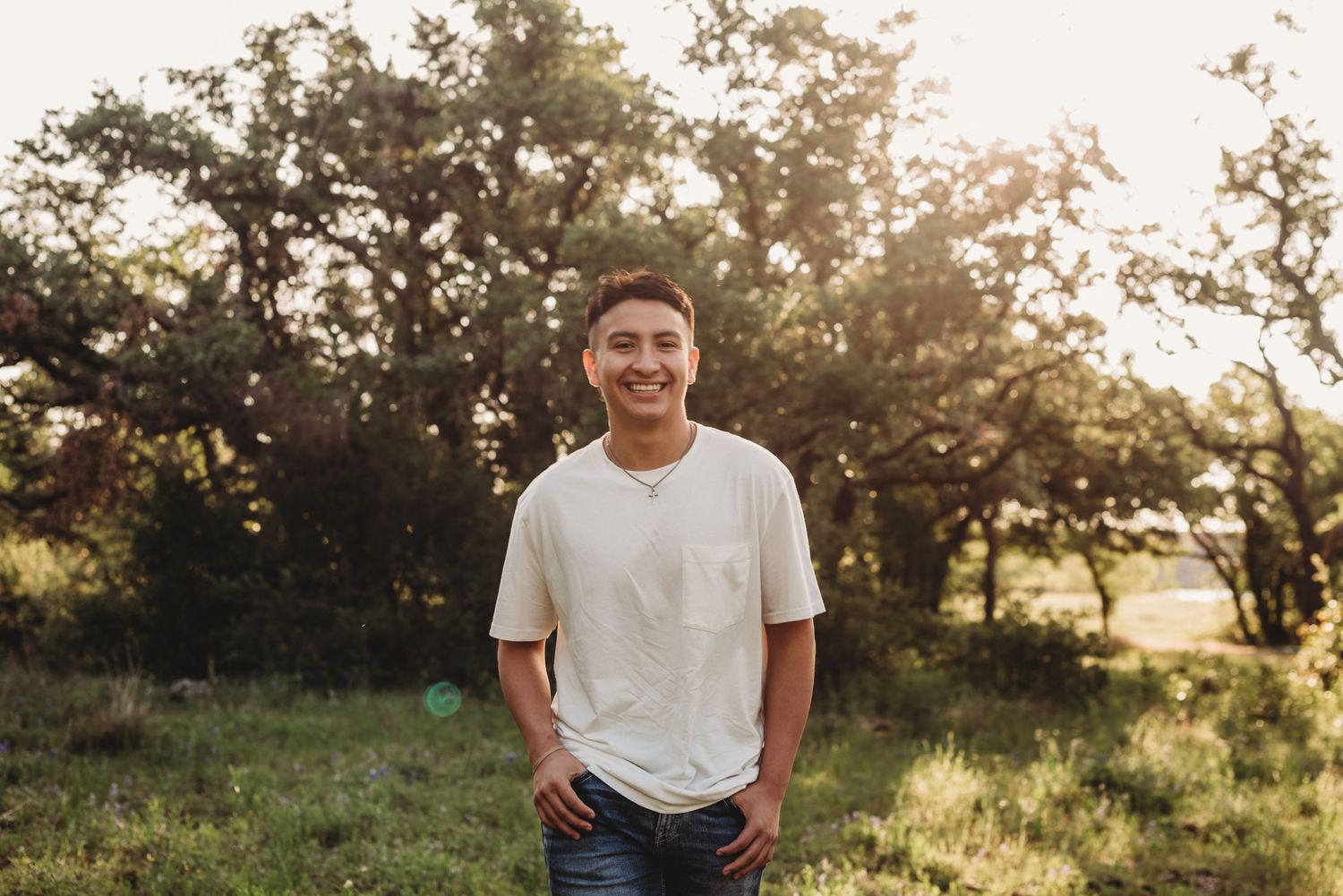 Young man in white t-shirt smiles at camera during outdoor portrait session at sunset.