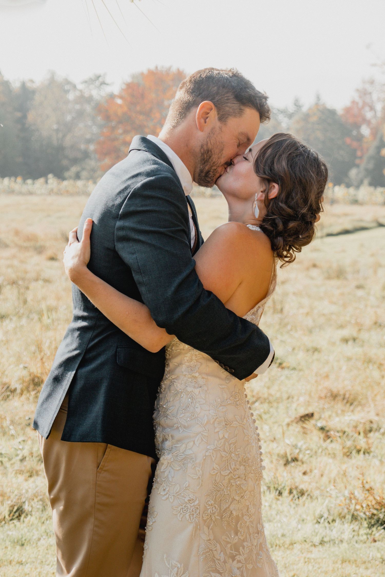 Wedding Photos Romantic couple sharing an intimate kiss in a sunlit autumn field. Southern NH