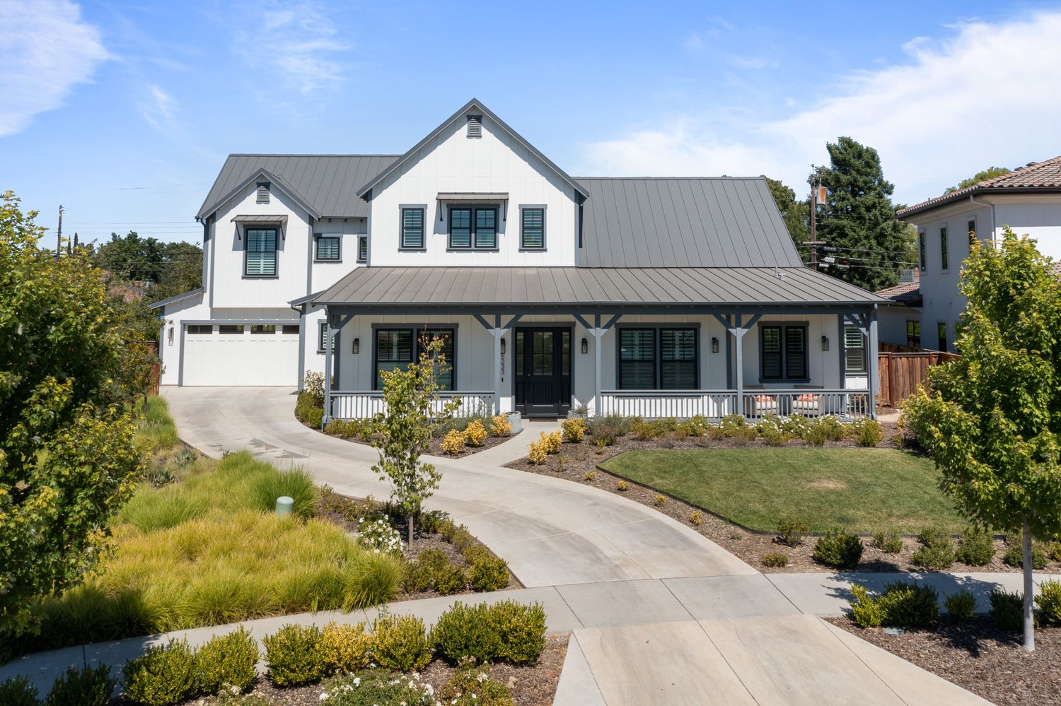 Modern farmhouse style home with white exterior, metal roof, and curved driveway on landscaped property.