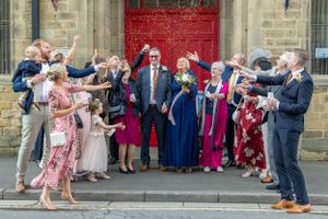 A festive wedding party celebrates outside a church with a bright red door. Bakewell Registry Office.