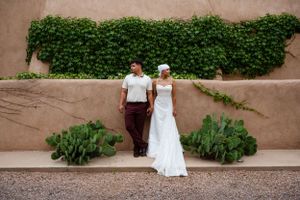 A wedding couple poses against an adobe wall with climbing green vines.