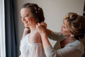 An intimate moment between mother and daughter during wedding preparations by a sunlit window.