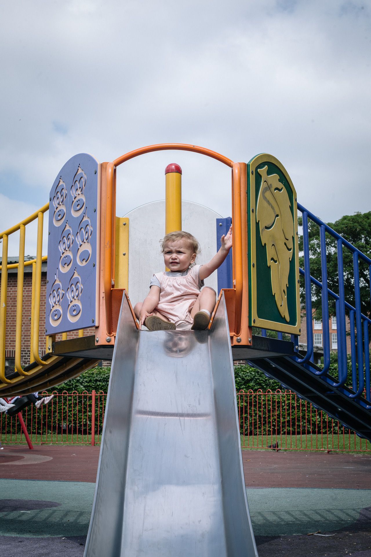 A child enjoys sliding down a colorful playground slide on a cloudy day.