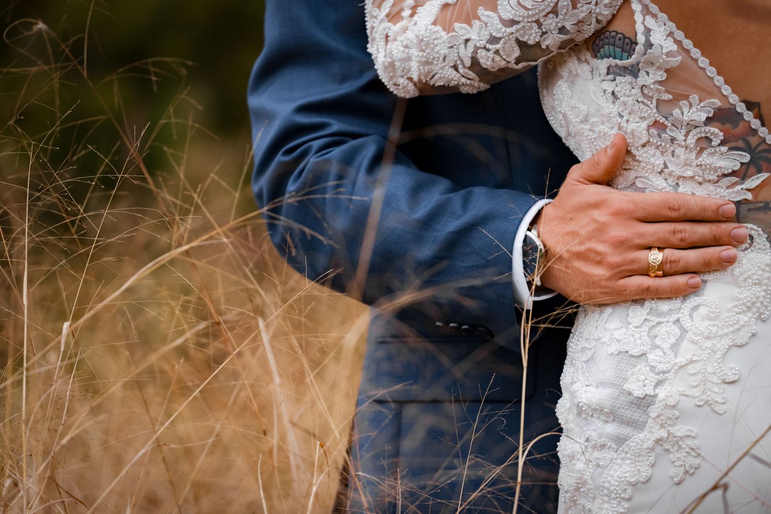 Close-up detail shot of lace wedding dress against navy suit during intimate moment.