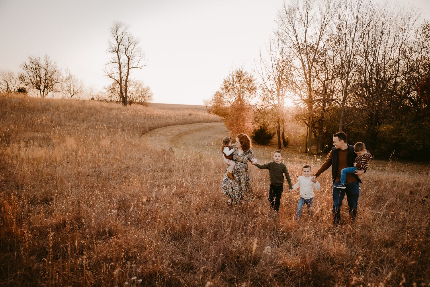 Family holding hands walking through golden autumn field at sunset.