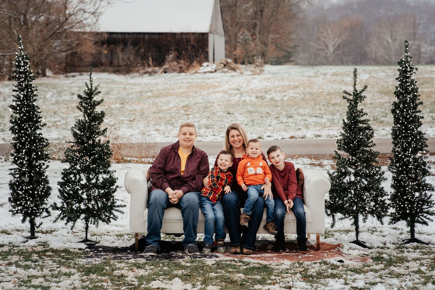 A family sitting on a bench surrounded by evergreen trees in winter with snowy ground.