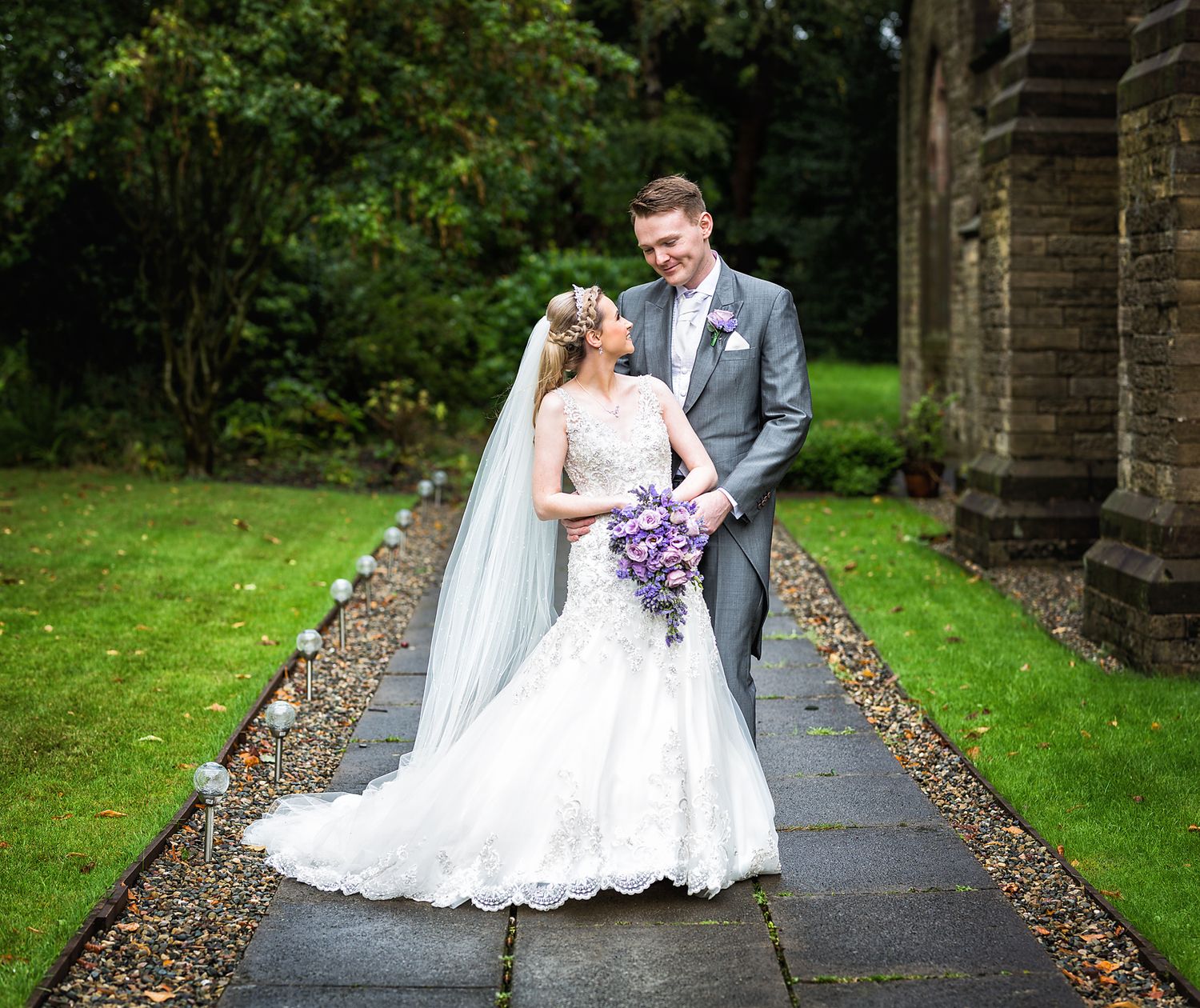 Blonde haired bride in white wedding dress looking at her smartly suited groom outside church
