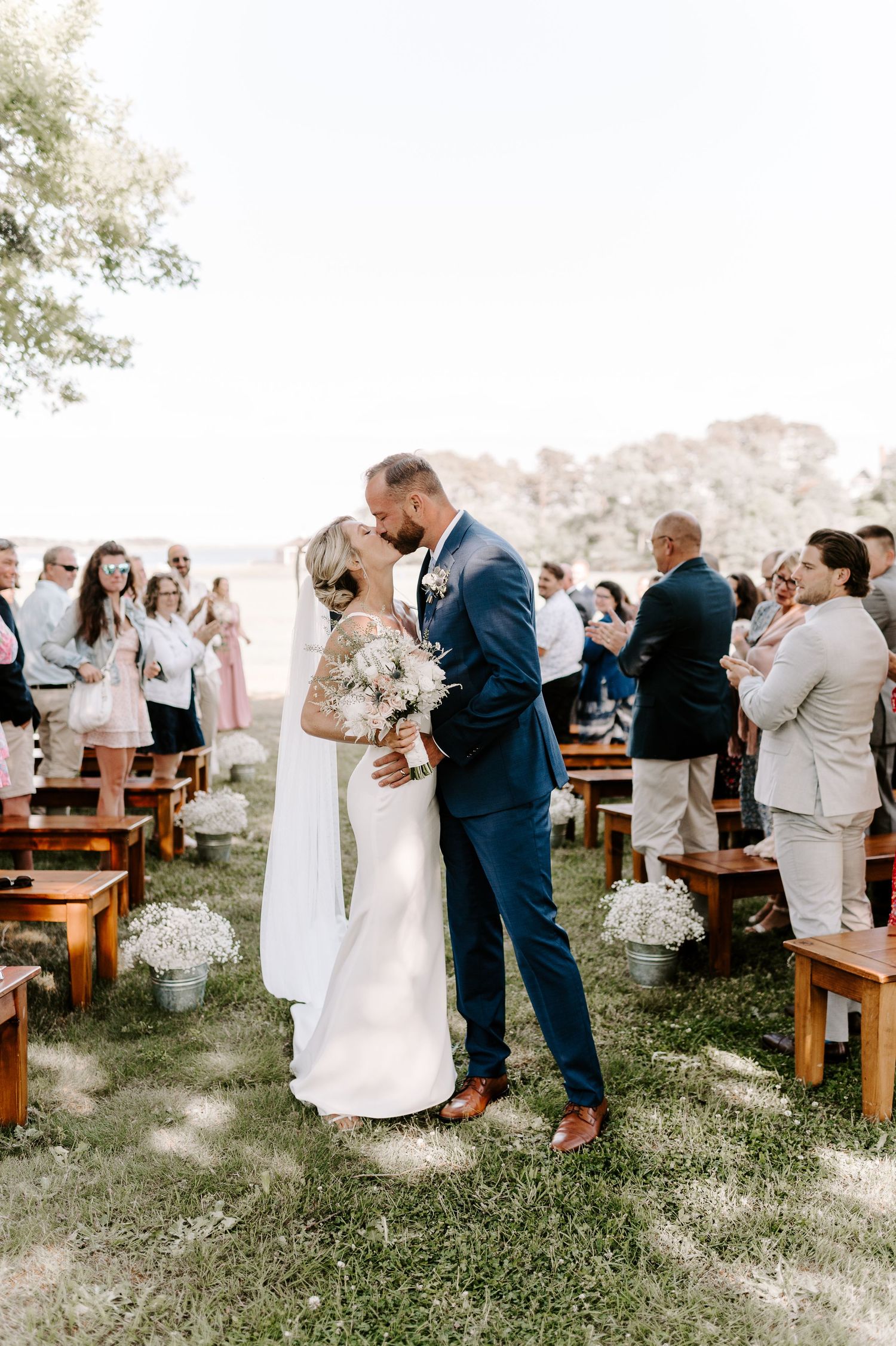 Wedding ceremony attendees celebrate on a scenic grassy hilltop with wooden bench seating.