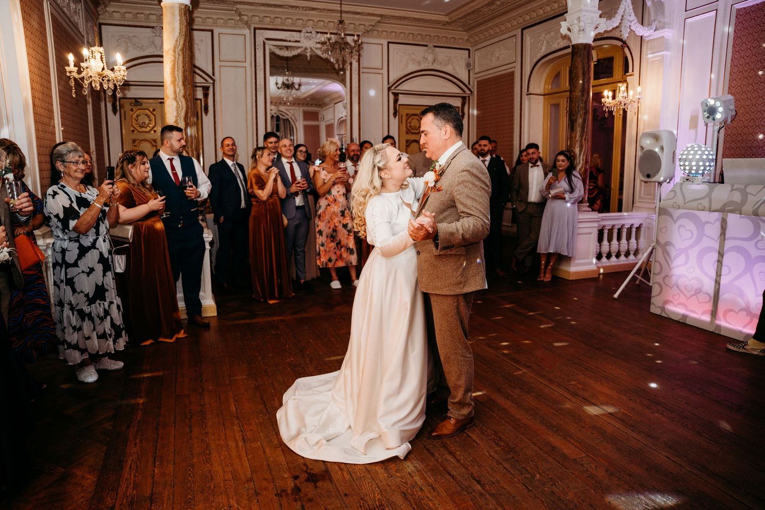 Romantic first dance moment in an ornate ballroom with warm lighting and gathered guests.
