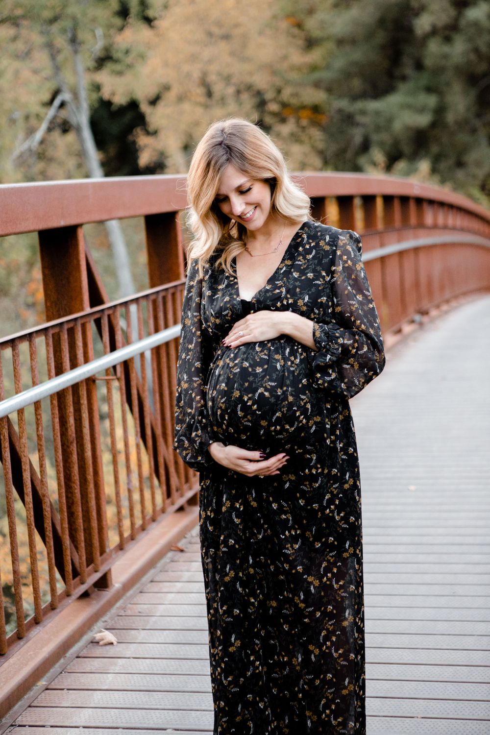 Maternity portrait on wooden bridge with black patterned dress during autumn season.