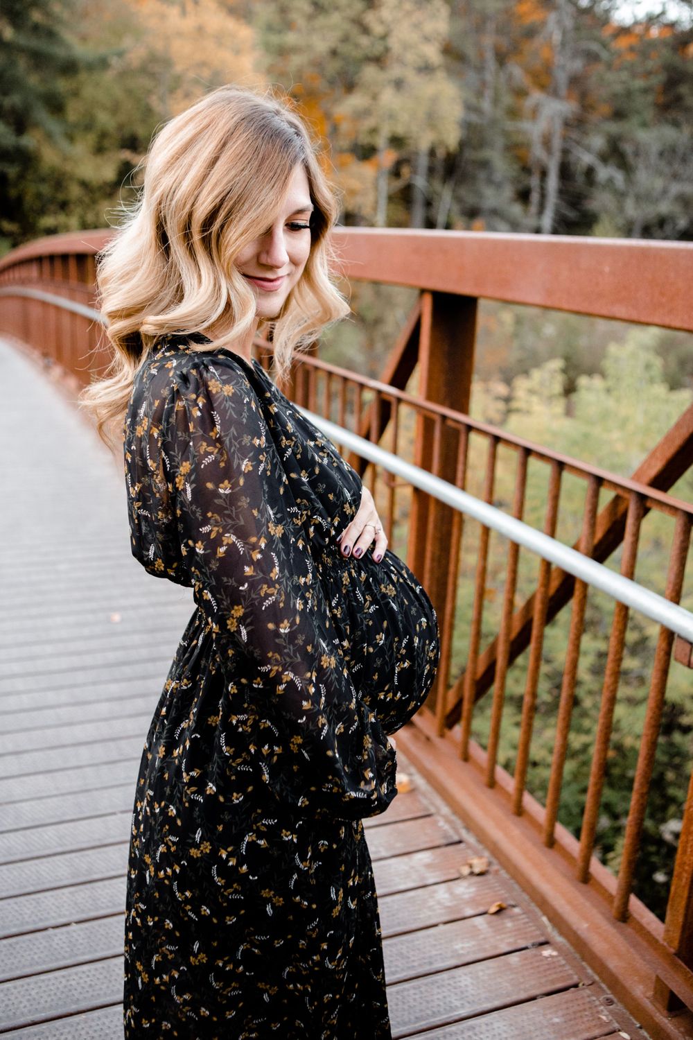 Joyful maternity portrait on wooden bridge with black flowing dress in autumn setting.