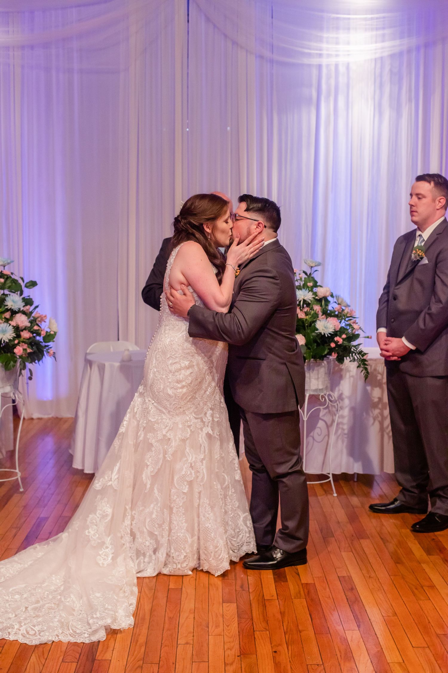 Romantic wedding ceremony moments unfold against purple-lit backdrop and hardwood floors.