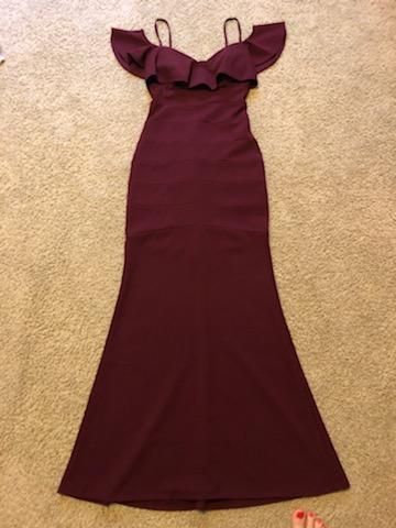 Burgundy off-shoulder mermaid gown with ruffle detail laid flat on carpet.