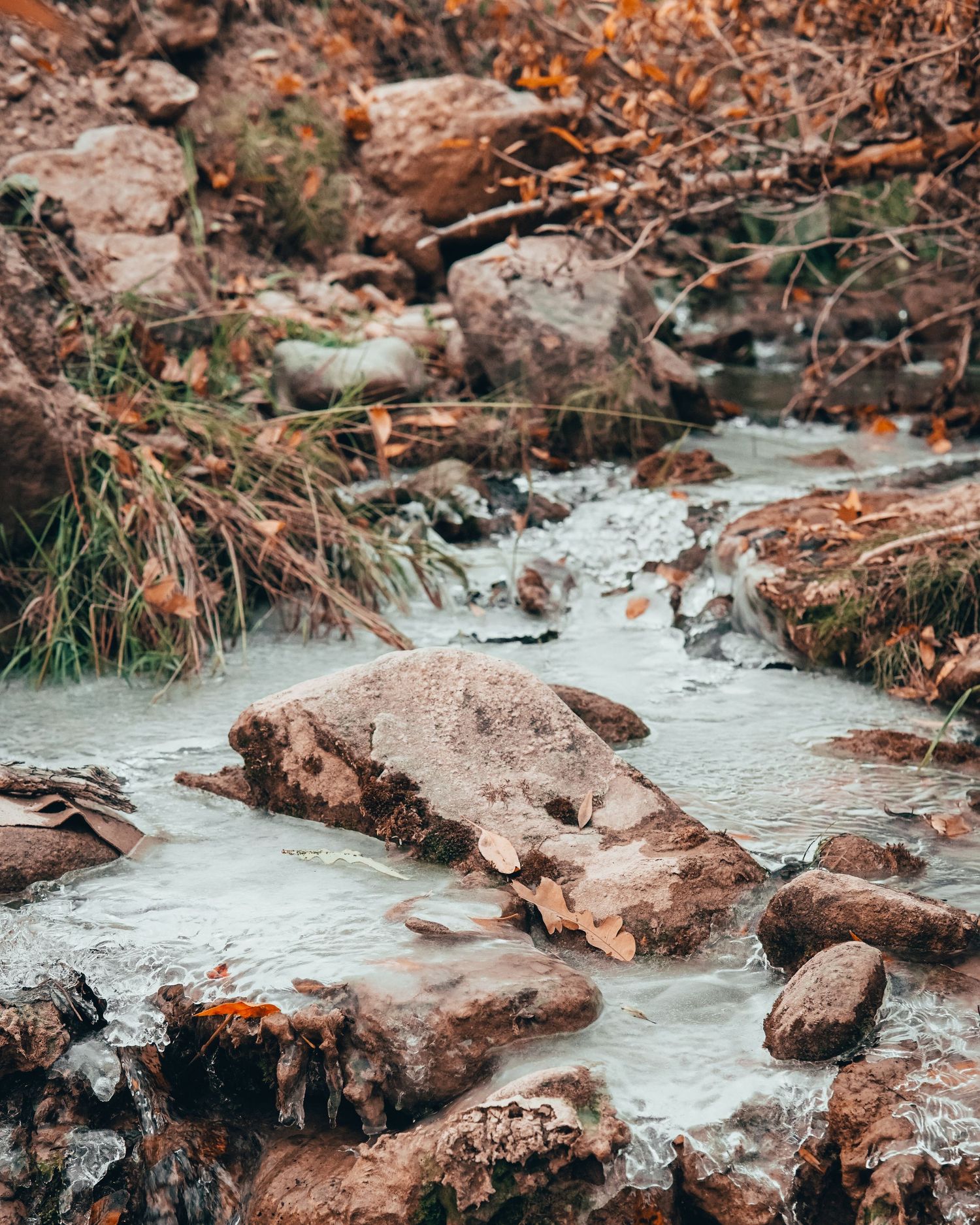 Rocky stream with turquoise water flowing through red rocks and autumn foliage.