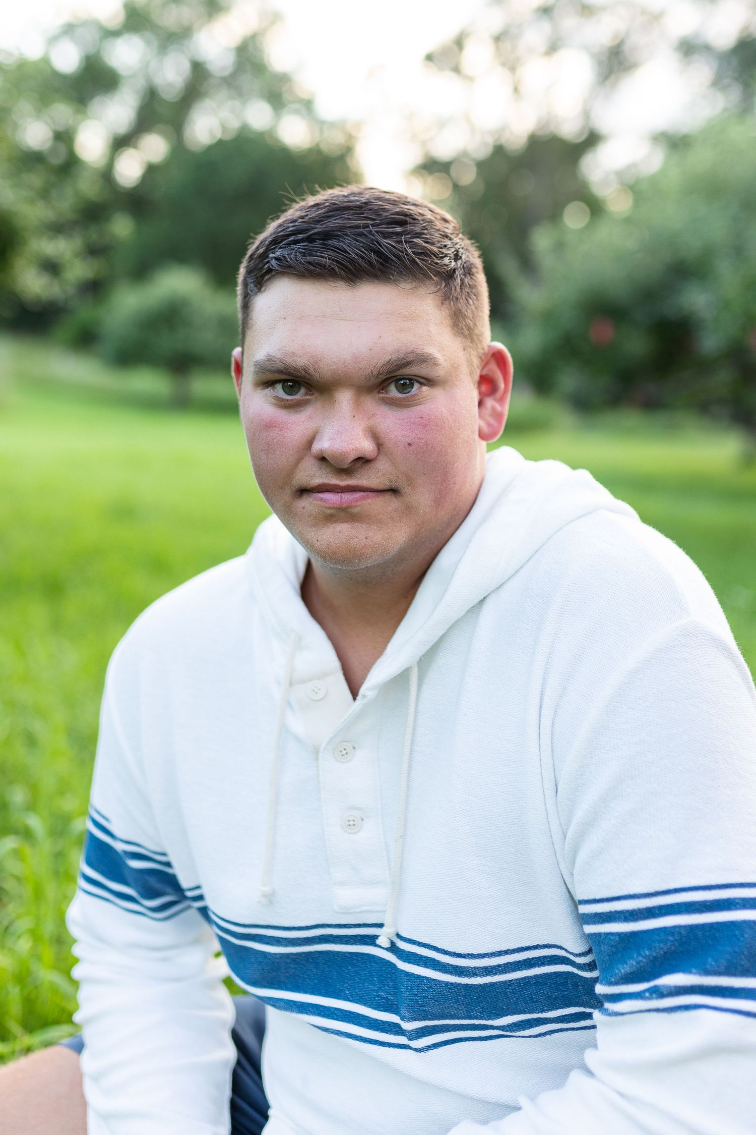 Senior portrait- young man with brown hair wearing a white dress shirt in a green field of trees.