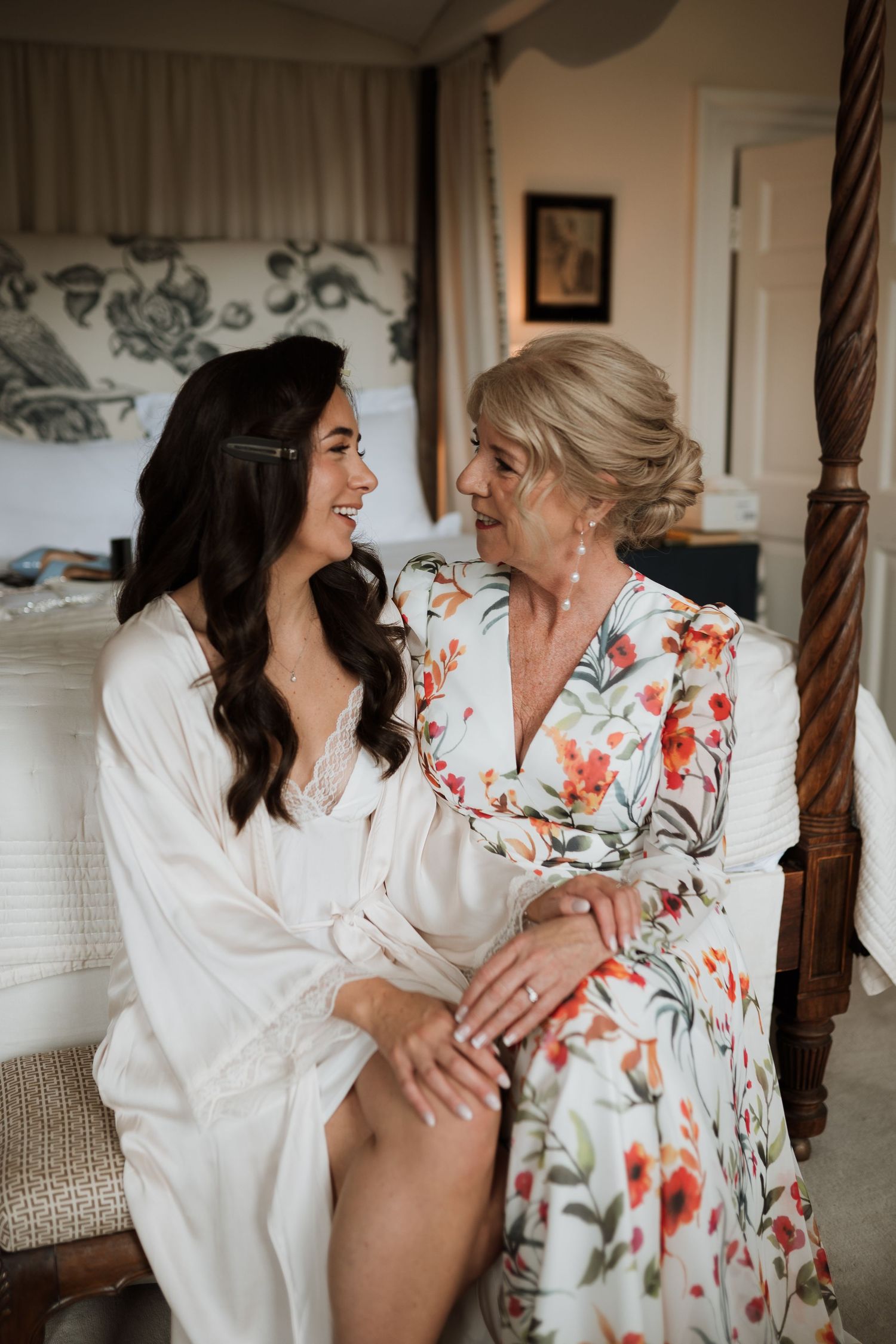 A bride and older woman share a joyful moment while getting ready.