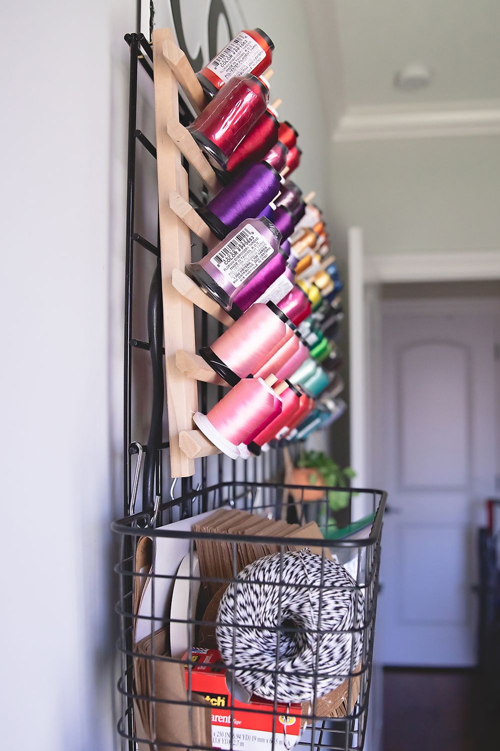 Colorful spools of thread arranged on a wall-mounted rack with storage basket below.
