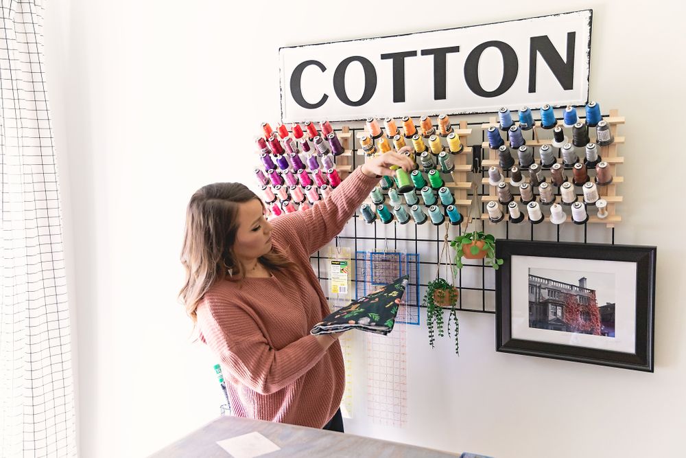 Person selecting thread from a colorful wall-mounted thread organizer labeled 'COTTON'.