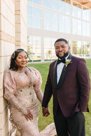 A couple poses outdoors at their wedding, with the bride in a beaded pink gown and groom in burgundy tuxedo.
