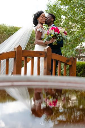 Romantic bridge moment with reflection in water and colorful floral bouquet.