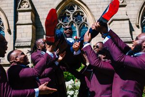 Groomsmen in purple suits playfully pose together outside a church.