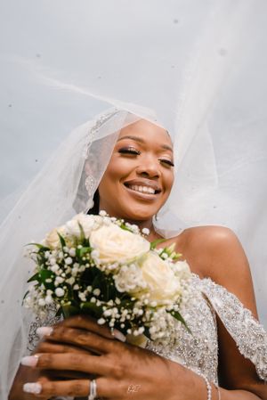 Radiant bride holding white roses and baby's breath bouquet with flowing veil.