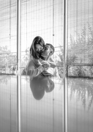 A couple embraces by reflective windows in a romantic black and white portrait.