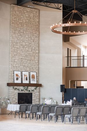 An elegant event space with stone walls, modern chandelier, and rows of grey chairs.