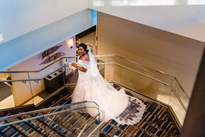 Bride in flowing white dress descending modern staircase in dramatic lighting.