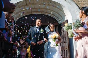 Wedding party exits church under shower of confetti while guests celebrate.