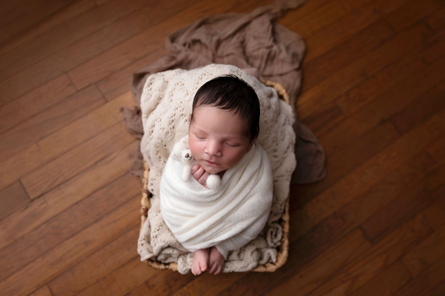 Sleeping baby wrapped in white swaddle on textured blanket and wooden floor.