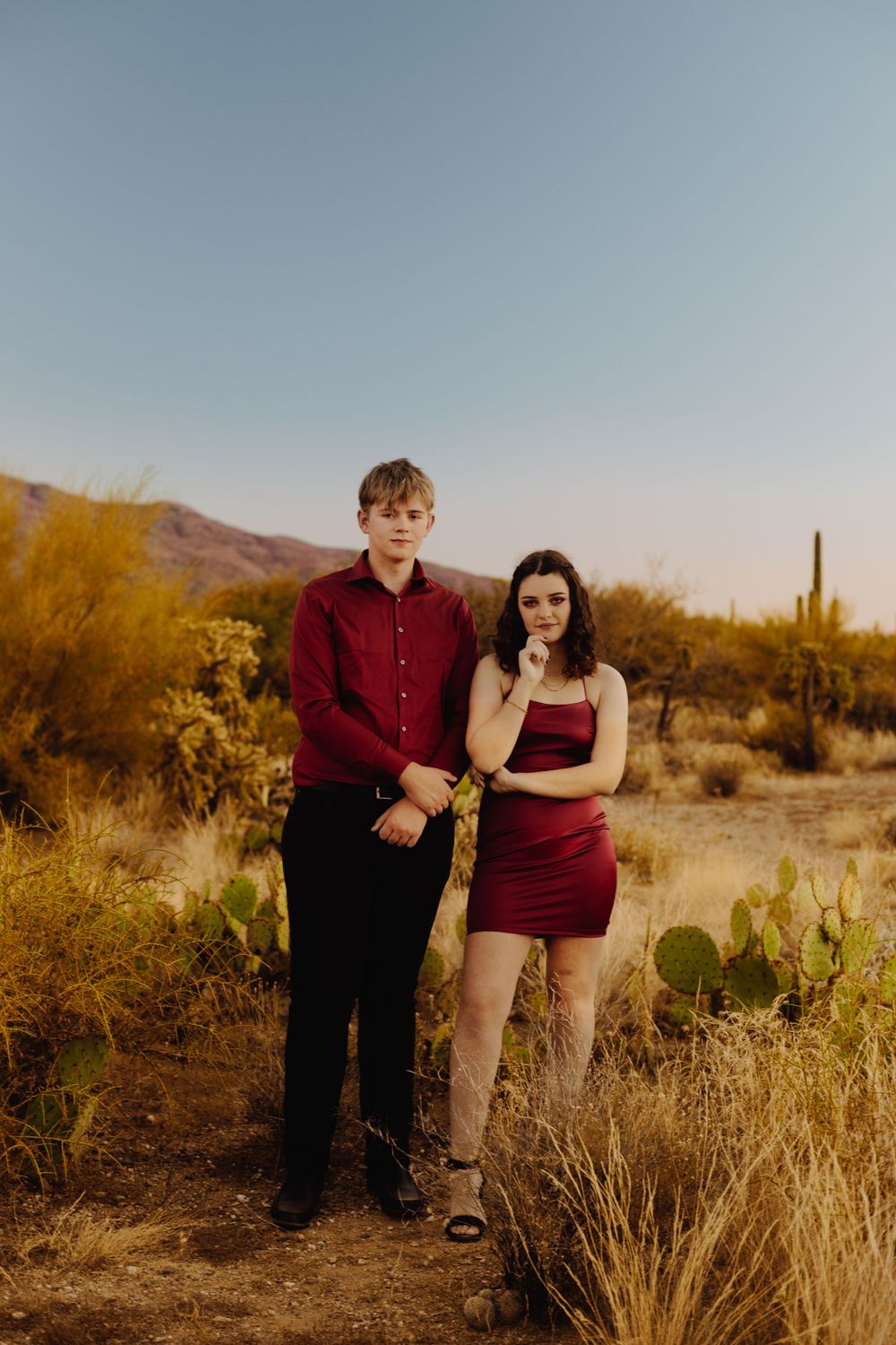 A couple poses in formal wear among desert plants during golden hour.