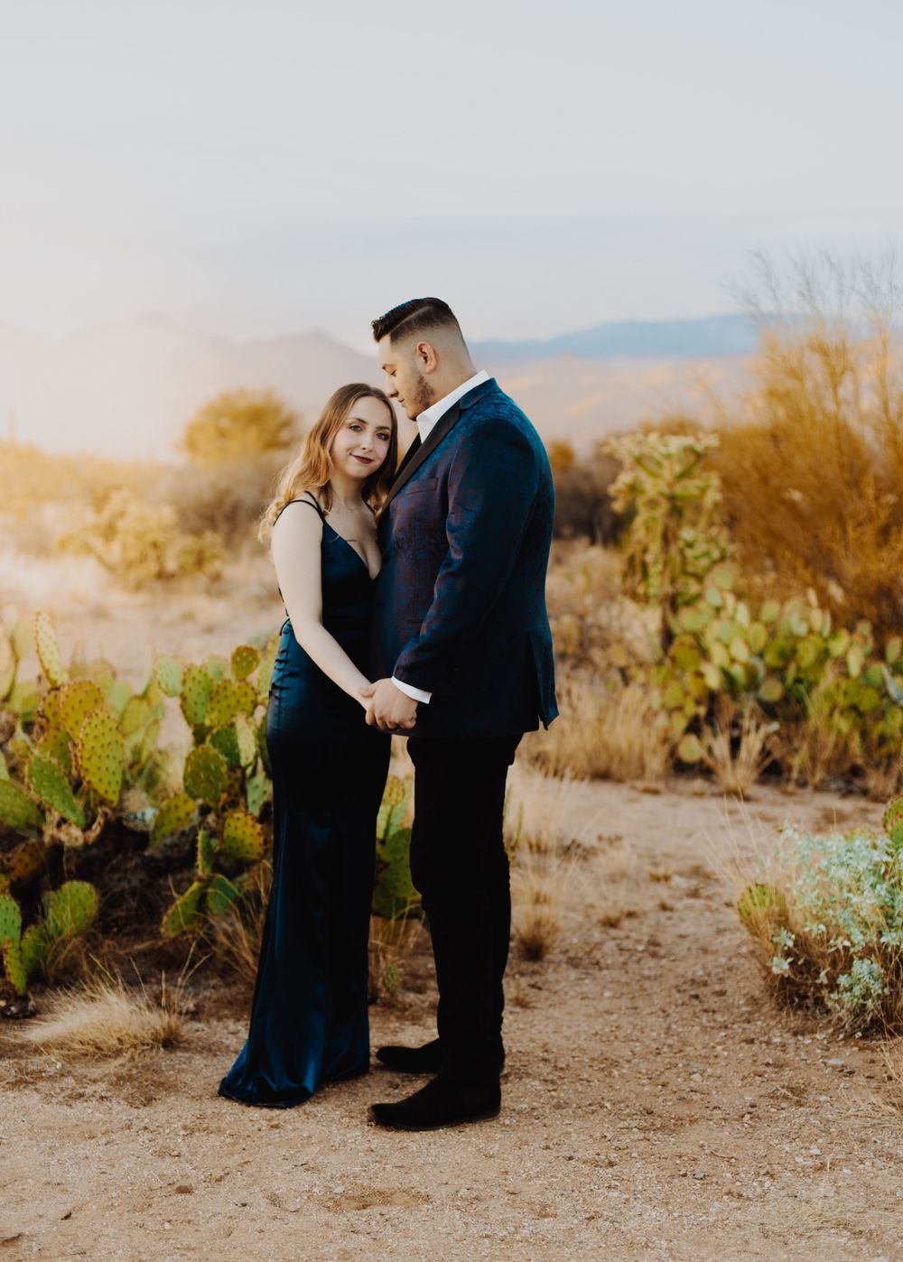 Engagement session in desert setting with cacti and mountains in background.